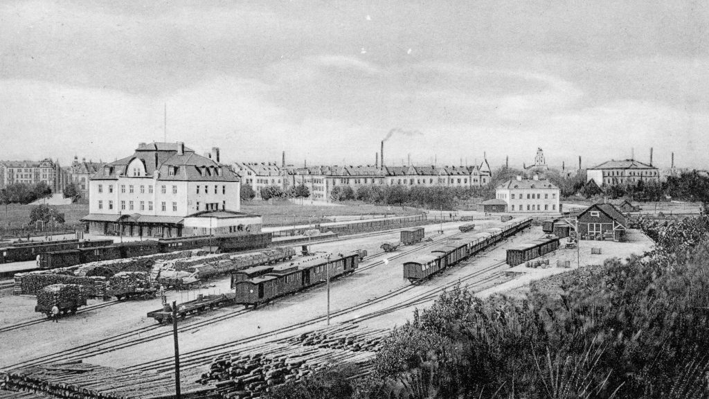 Vy från Oxelbergen över Östra stations nya och gamla stationshus. Vykort i Norrköpings stadsarkivs samlingar
